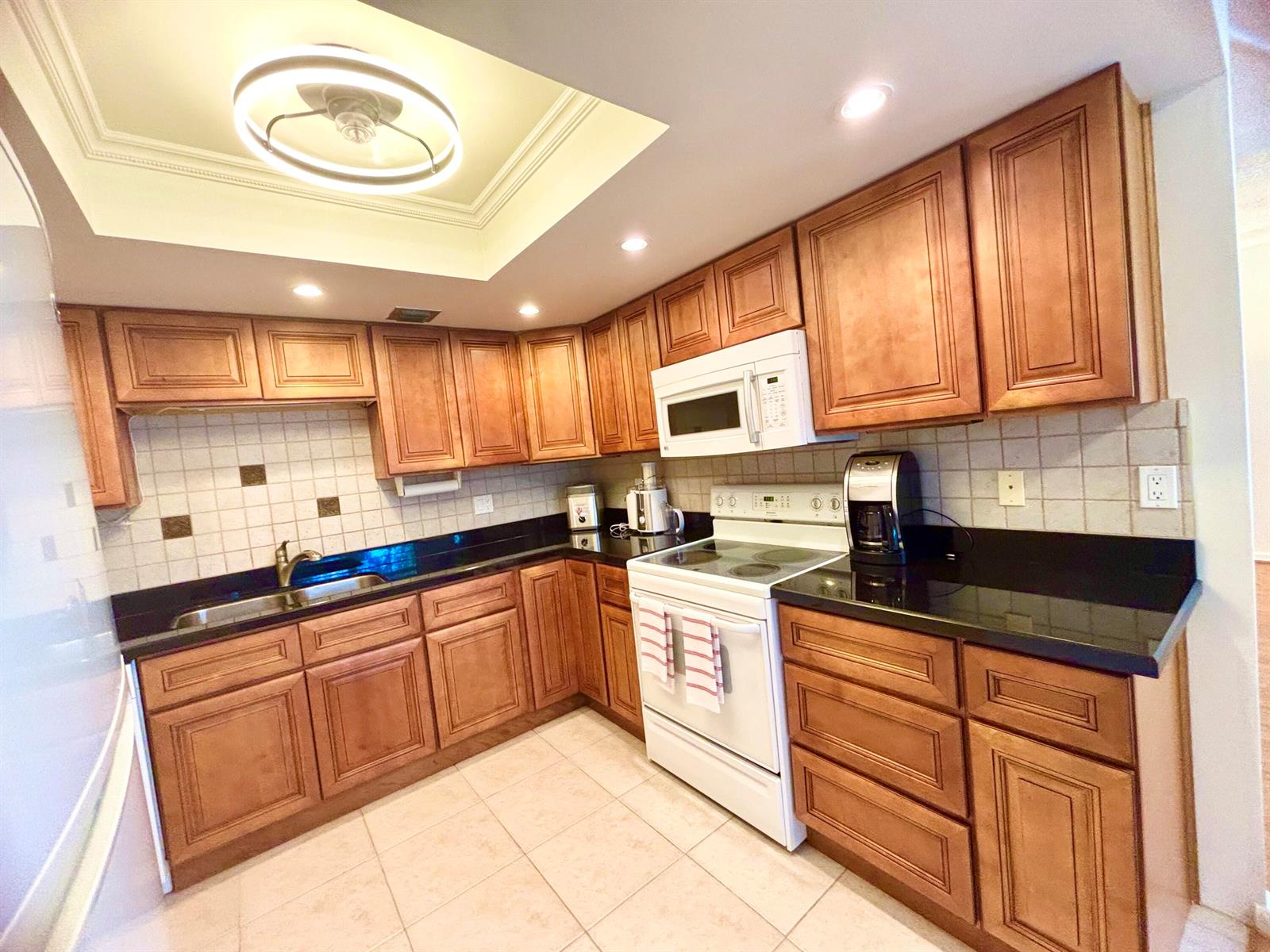 A kitchen features wood cabinets, black countertops, white appliances, and a recessed ceiling light — 2069 Oakridge F Unit 2069, Deerfield Beach FL 33442, DEERFIELD BEACH, FL