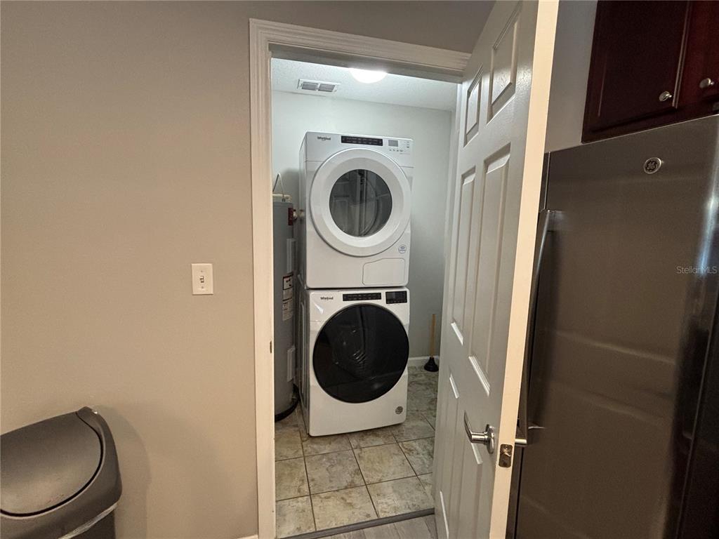 A laundry closet contains a stacked washer and dryer unit next to a water heater — 14501 GROVE RESORT AVENUE UNIT 1224, WINTER GARDEN, FL