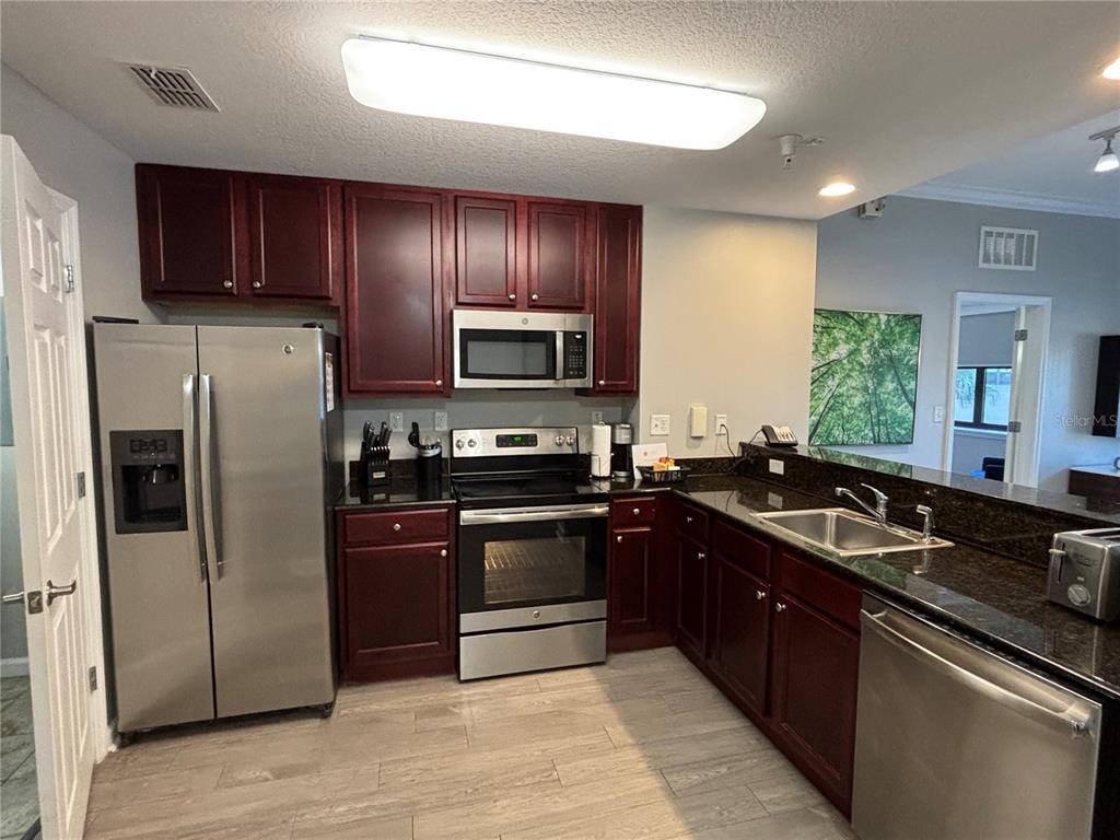 A kitchen features dark wood cabinets, stainless steel appliances, and granite countertops — 14501 GROVE RESORT AVENUE UNIT 1224, WINTER GARDEN, FL