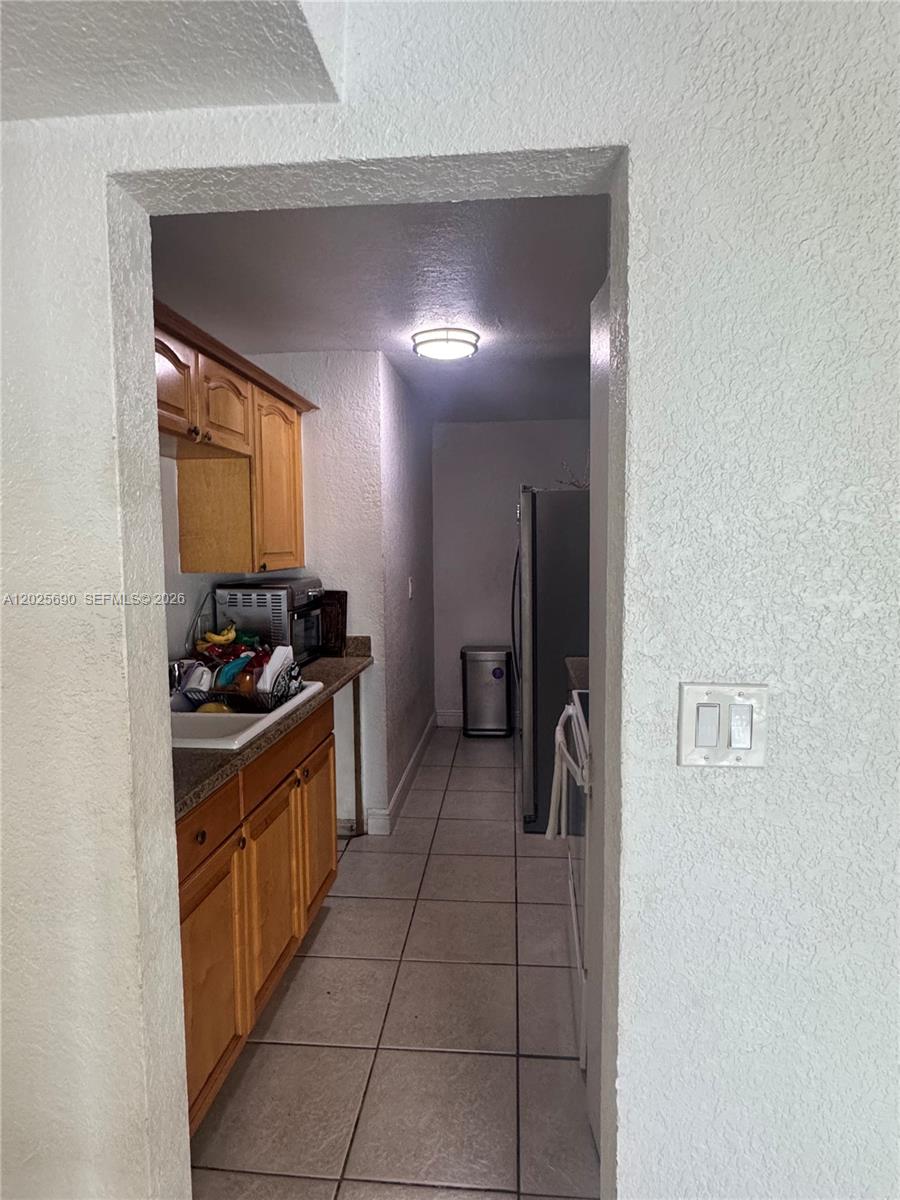 A narrow galley kitchen features light wood cabinets, tiled floors, and a stainless steel refrigerator — 7235 SW 94th Pl # J6, Miami FL 33173, MIAMI, FL