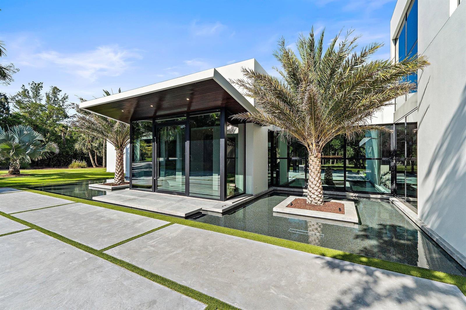 A modern house exterior features a flat roof, glass walls, and a reflecting pool — 12 N Beach Road, Jupiter Island FL 33455, JUPITER ISLAND, FL