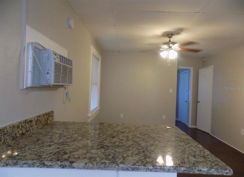 A kitchen counter with granite countertops overlooks a room with a ceiling fan and AC — 626 HIGHLAND STREET N, ST PETERSBURG, FL