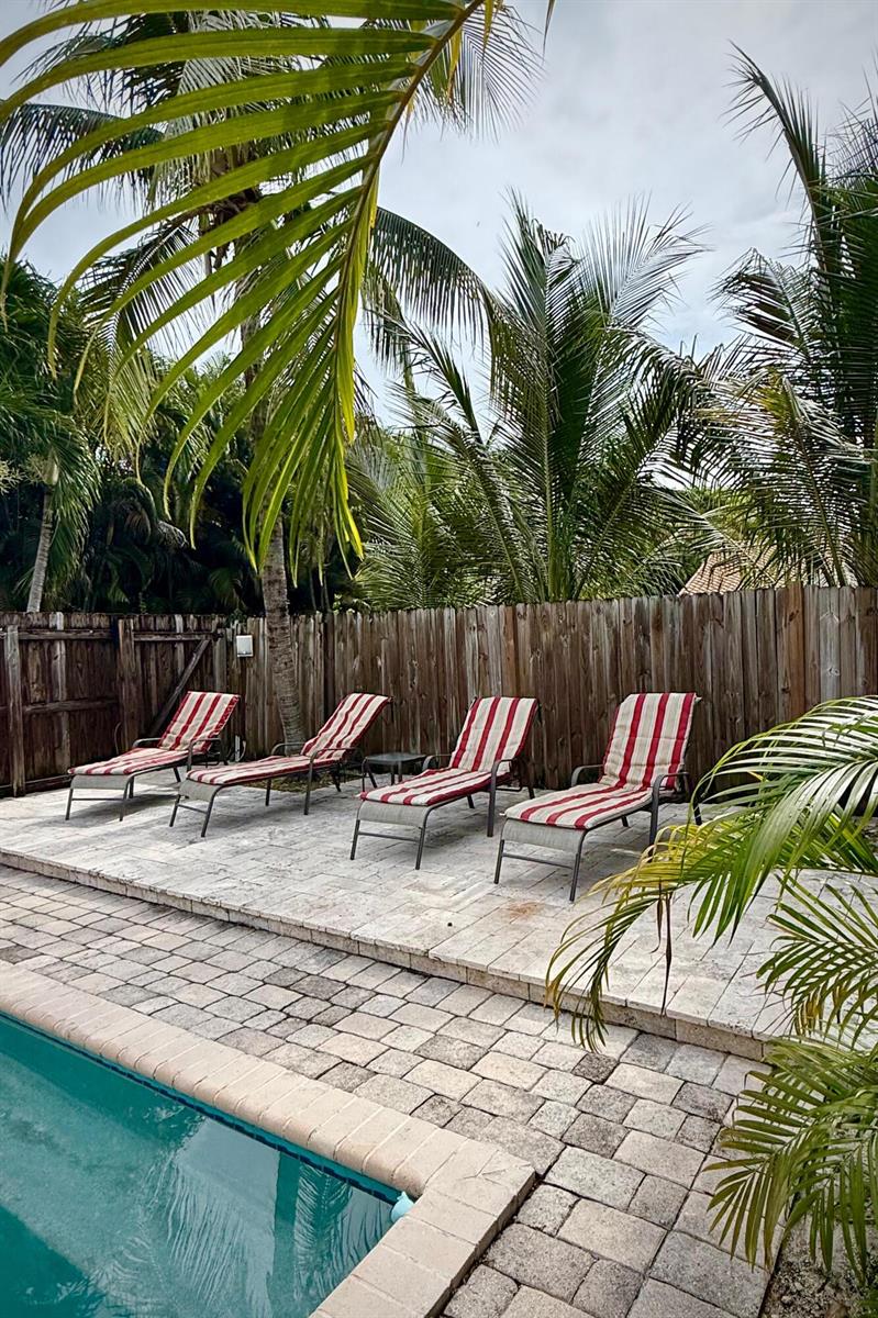 Four striped lounge chairs sit on a stone patio beside a swimming pool and fence — 619 NE 7th Avenue, Delray Beach FL 33483, DELRAY BEACH, FL