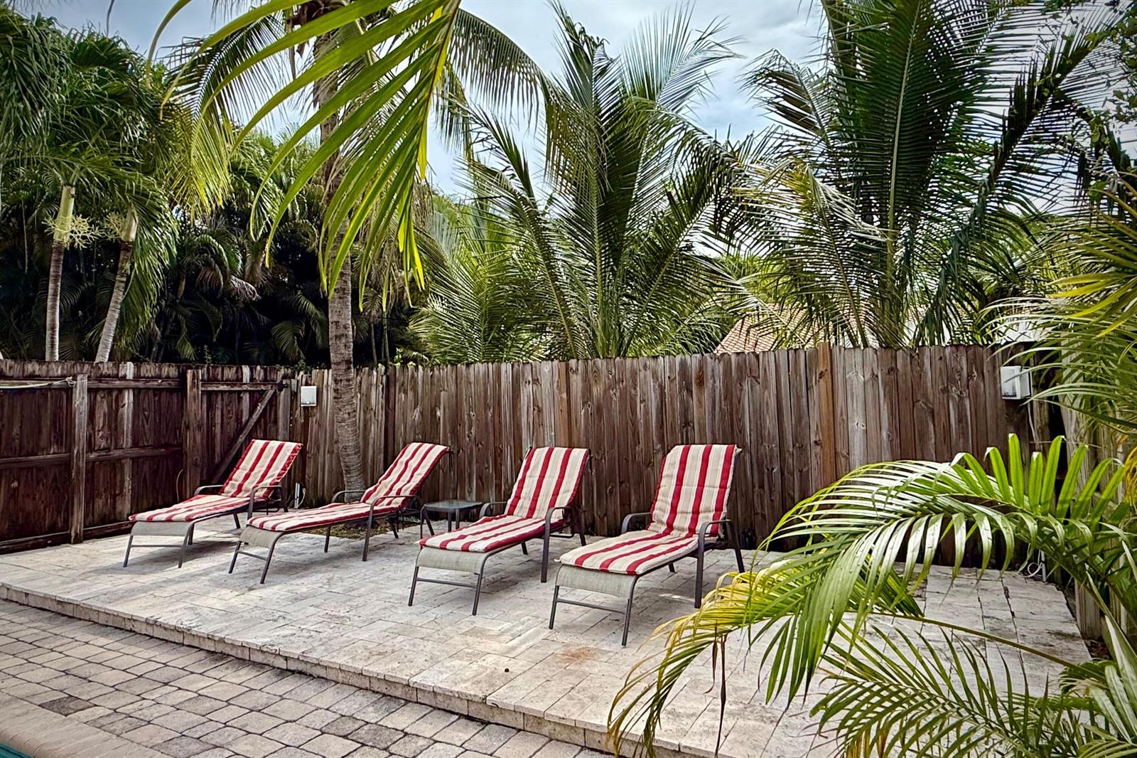Four striped lounge chairs sit on a stone patio in front of a wooden fence — 619 NE 7th Avenue, Delray Beach FL 33483, DELRAY BEACH, FL