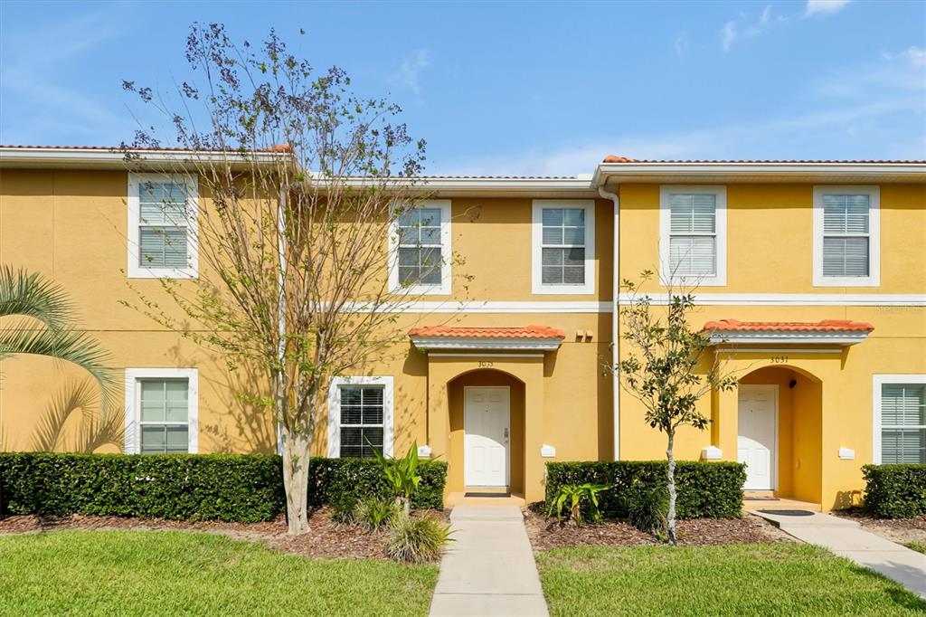 A two-story yellow townhouse exterior with white trim, tiled roofs, and two front entrances — 3033 BIRD OF PARADISE LANE, KISSIMMEE, FL