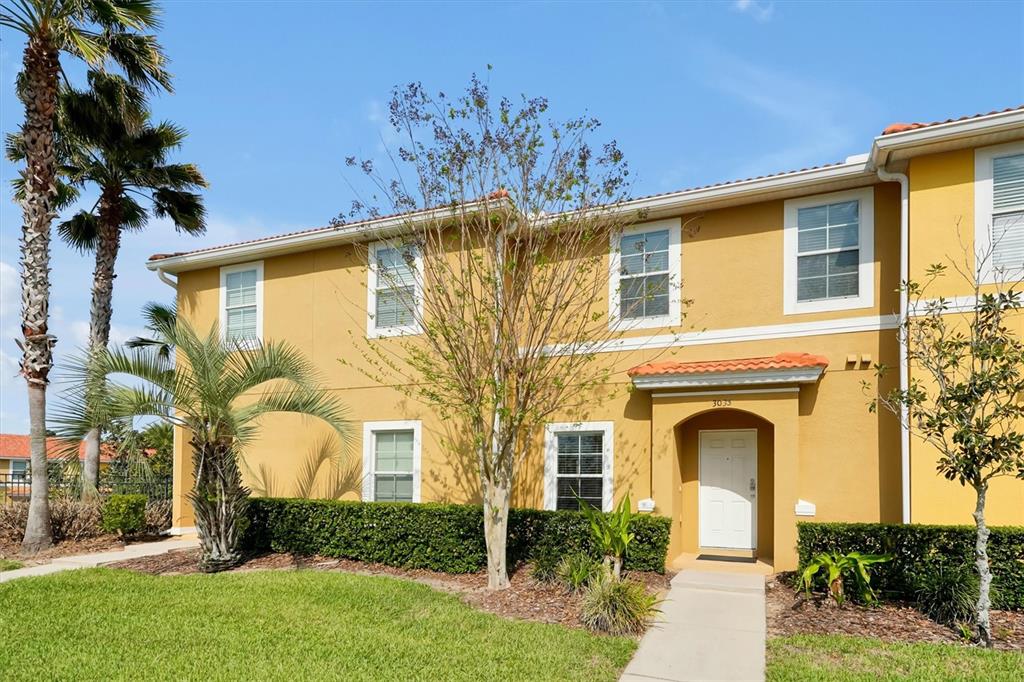 A two-story yellow stucco townhouse with a white front door and a palm tree — 3033 BIRD OF PARADISE LANE, KISSIMMEE, FL