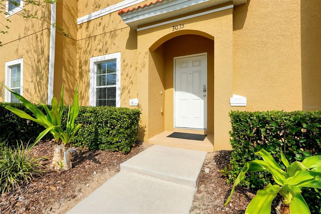A tan stucco building exterior features a white front door under a covered entryway — 3033 BIRD OF PARADISE LANE, KISSIMMEE, FL