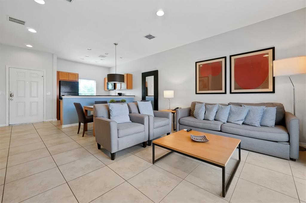 A living room with tile floors, a grey sofa, two armchairs, and an open kitchen — 3033 BIRD OF PARADISE LANE, KISSIMMEE, FL