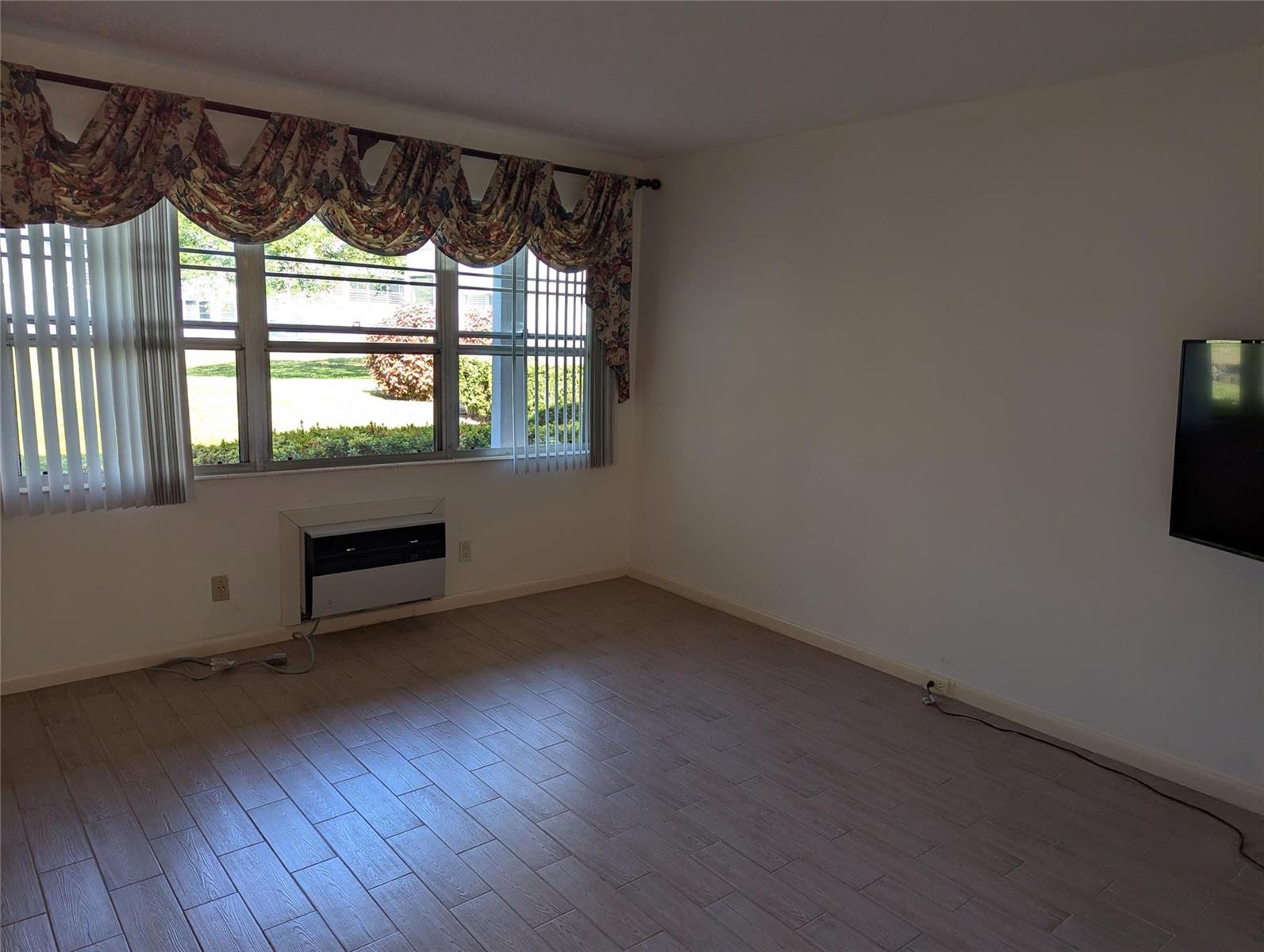 A living room with light wood-look tile flooring, a wall-mounted television, and a window unit — 190 Oakridge M, Deerfield Beach FL 33442, DEERFIELD BEACH, FL