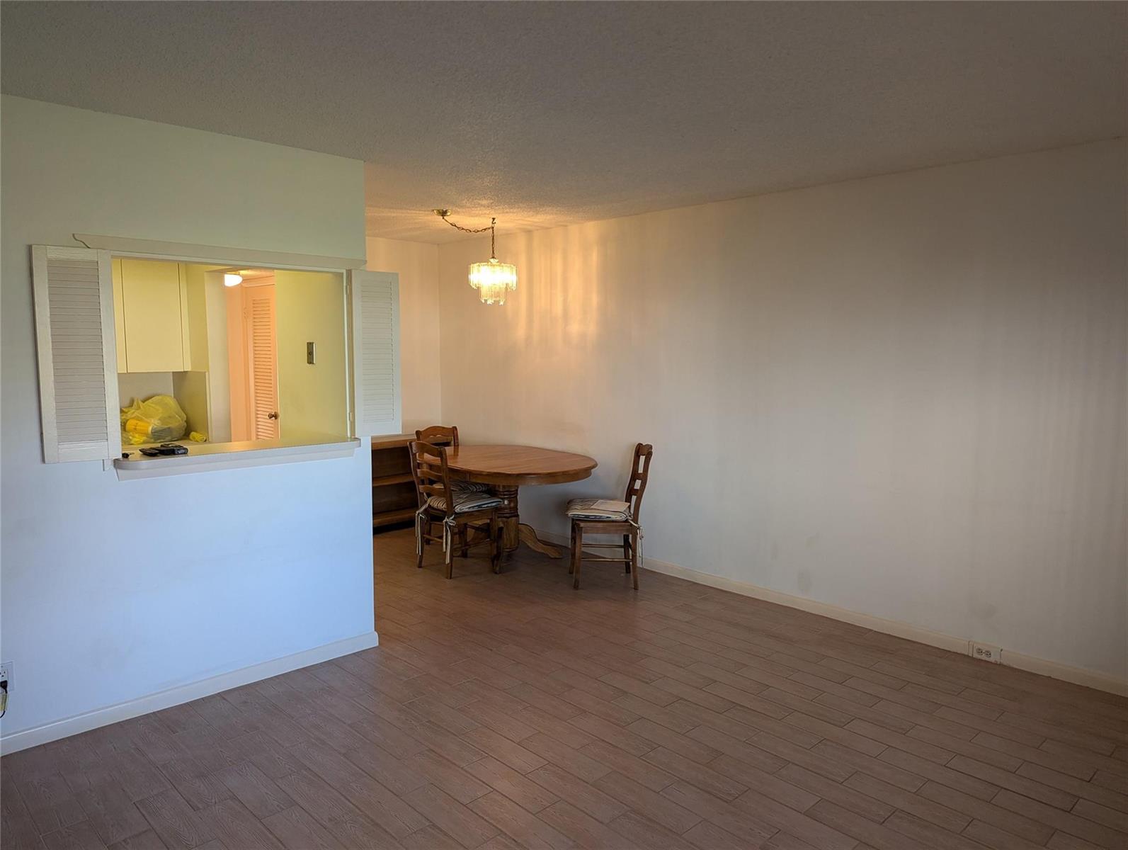 A dining area with a wood table, chairs, and a chandelier next to a kitchen pass-through — 190 Oakridge M, Deerfield Beach FL 33442, DEERFIELD BEACH, FL