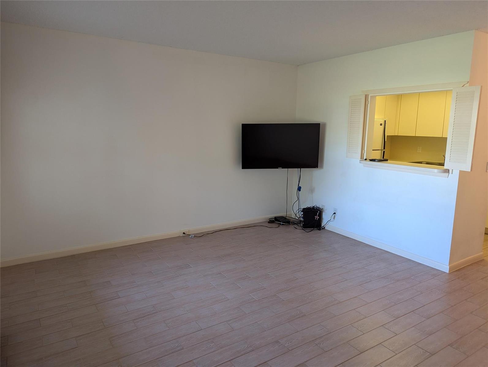 An empty living room with light wood-look tile flooring and a wall-mounted television — 190 Oakridge M, Deerfield Beach FL 33442, DEERFIELD BEACH, FL