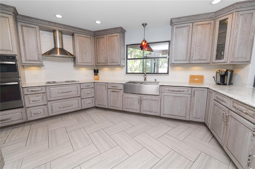 A kitchen features light wood cabinets, stainless steel appliances, a farmhouse sink, and herringbone flooring — 1224 RAINBROOK CIRCLE, VALRICO, FL