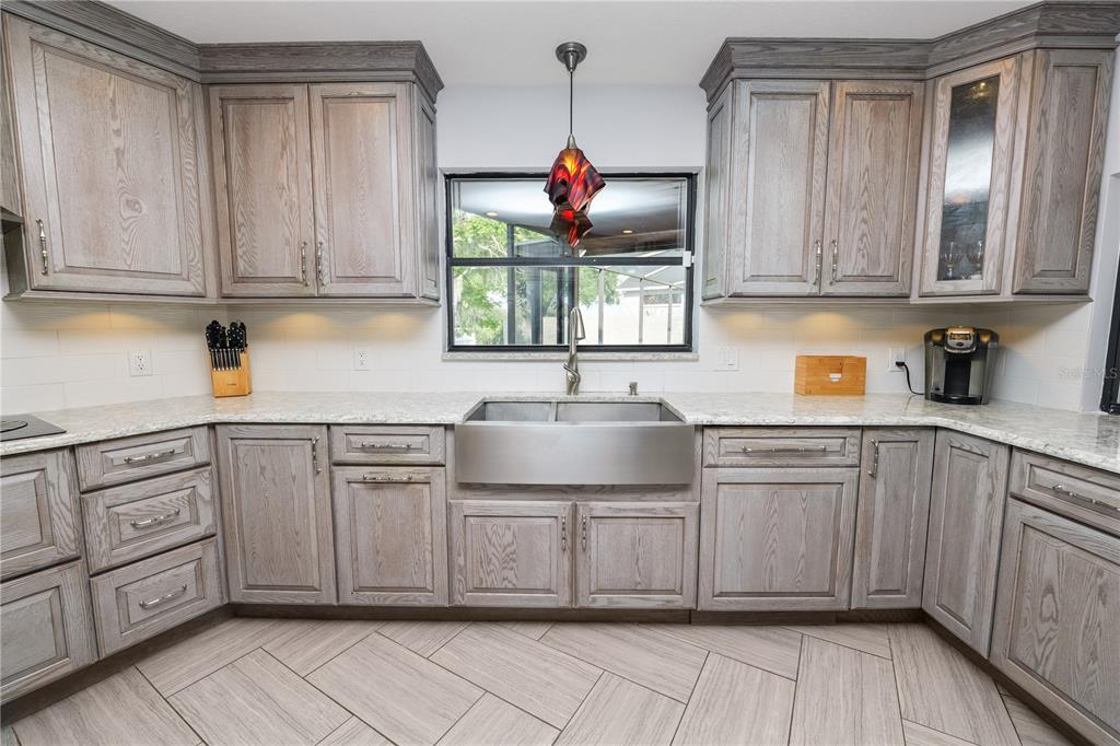 A kitchen features gray wood cabinets, a stainless steel farmhouse sink, and light countertops — 1224 RAINBROOK CIRCLE, VALRICO, FL