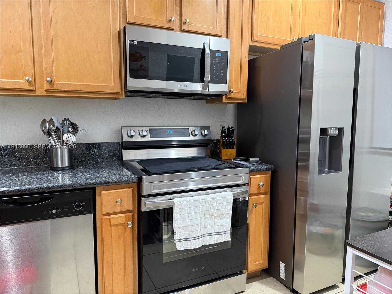 A kitchen features wooden cabinets, stainless steel appliances, and dark granite countertops — 8948 SW 19th St # 909, Miramar FL 33025, MIRAMAR, FL