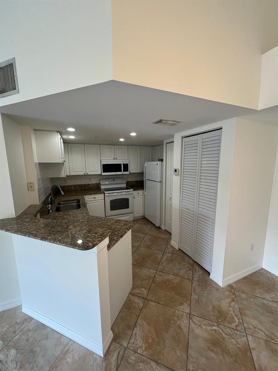 A kitchen features white cabinets, granite countertops, white appliances, and light-colored tile flooring — 500 Crestwood Court N # 517, Royal Palm Beach FL 33411, ROYAL PALM BEACH, FL
