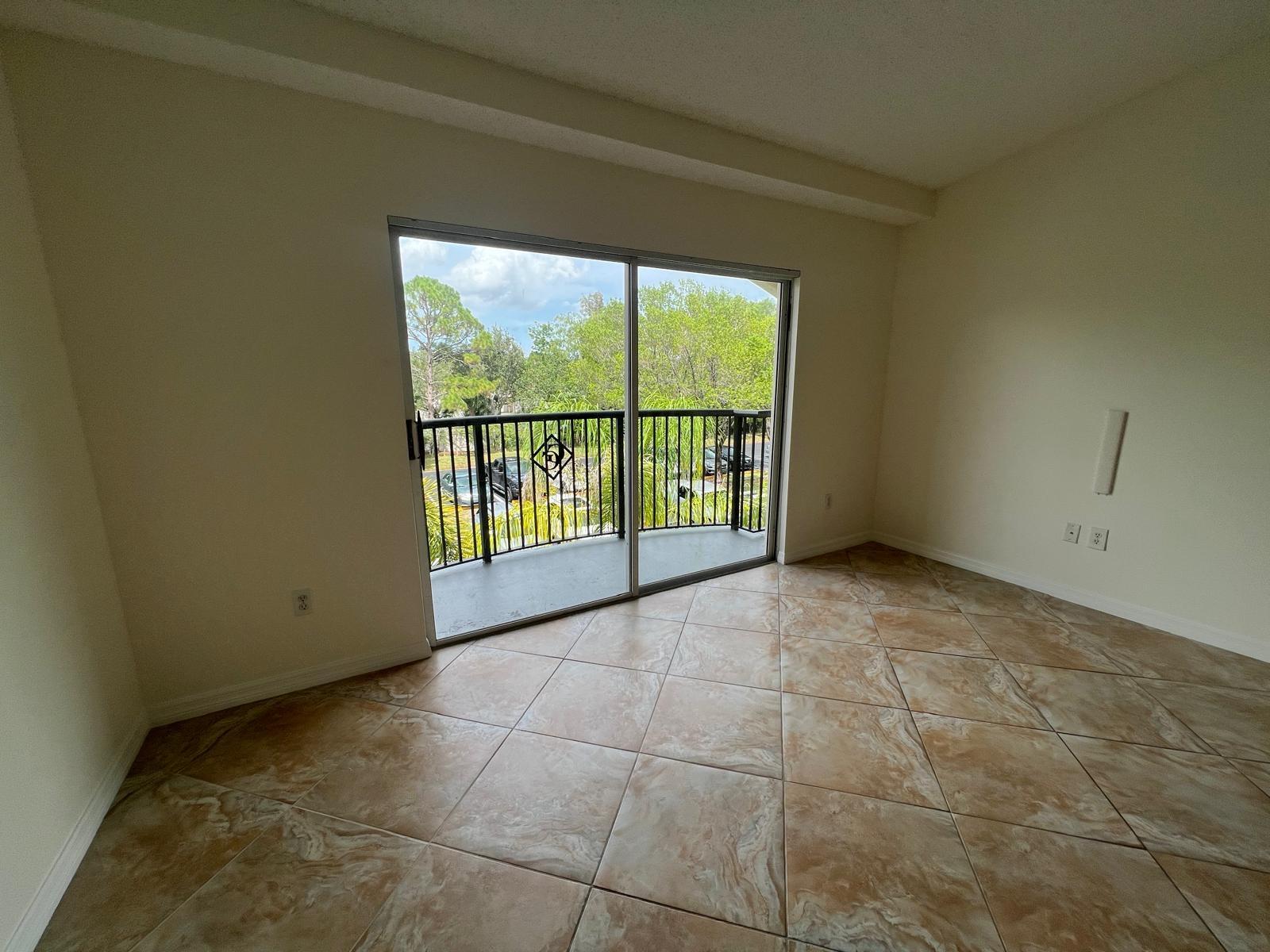 An empty room with tan tile flooring and a sliding glass door leading to a balcony — 500 Crestwood Court N # 517, Royal Palm Beach FL 33411, ROYAL PALM BEACH, FL