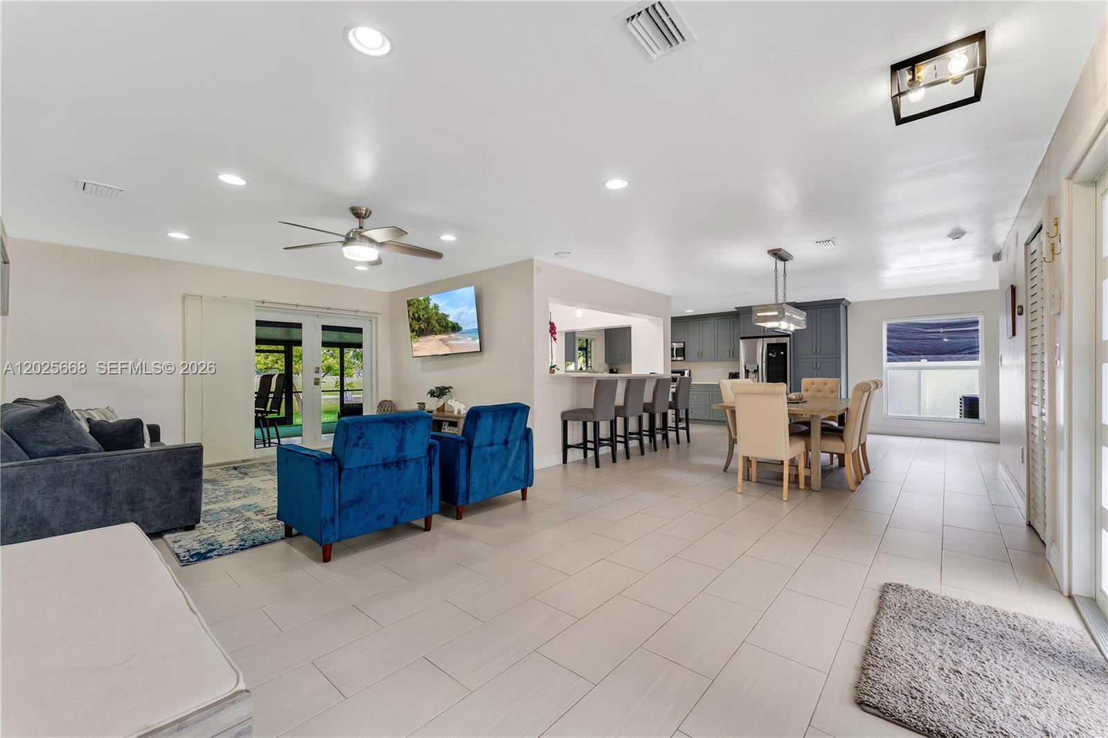 An open-concept living and dining area features tile flooring, blue armchairs, and a kitchen island — 9501 E Palmetto Club Ln E # 9501, Palmetto Bay FL 33157, PALMETTO BAY, FL