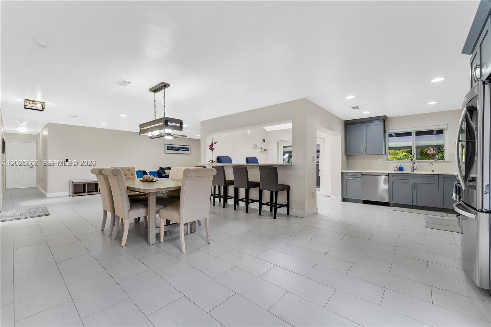 An open-concept kitchen and dining area features gray cabinetry, a breakfast bar, and tile flooring — 9501 E Palmetto Club Ln E # 9501, Palmetto Bay FL 33157, PALMETTO BAY, FL