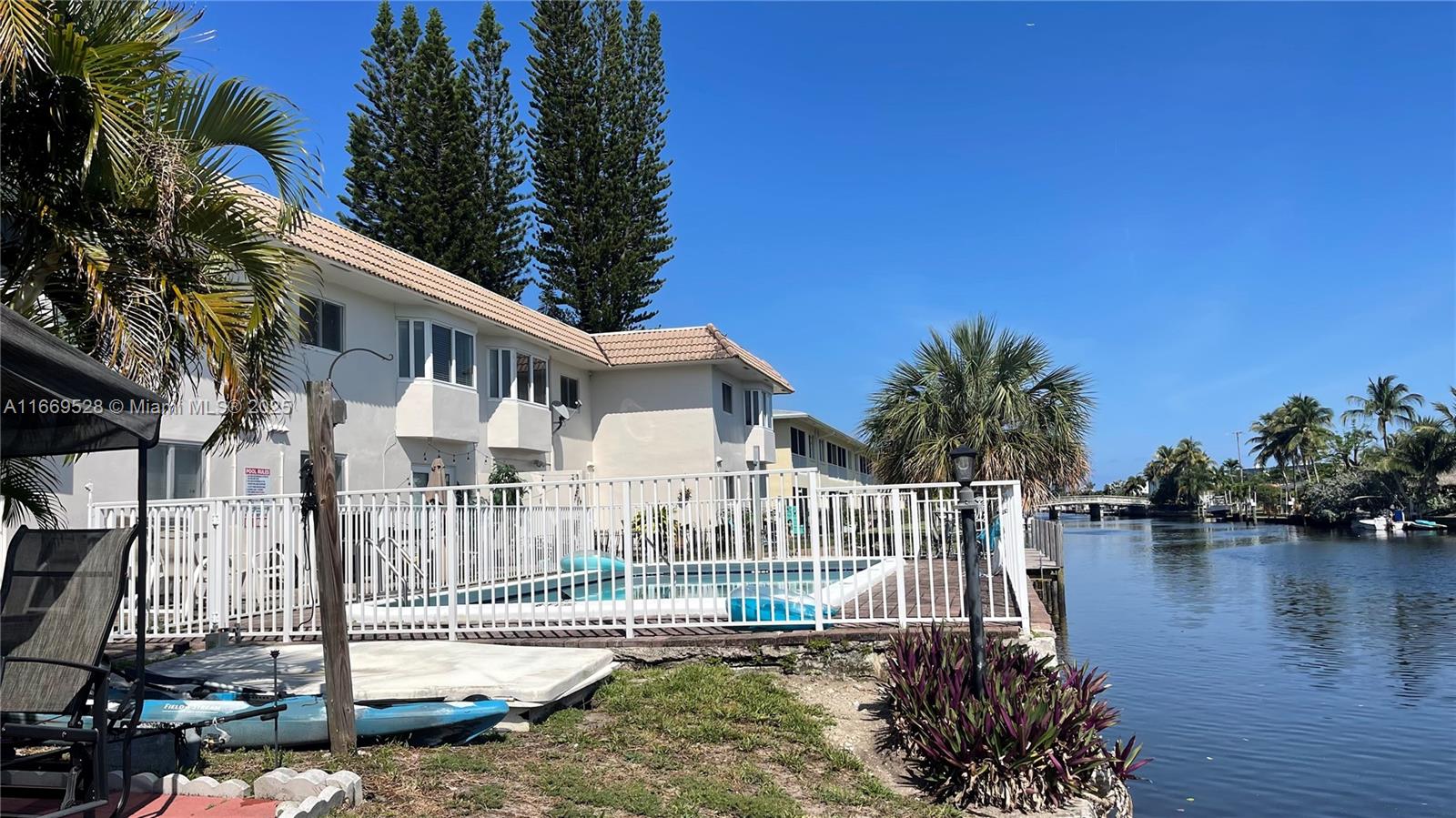 A white building with a swimming pool sits beside a canal under a clear sky — 840 Pine Dr # 103, Pompano Beach FL 33060, POMPANO BEACH, FL