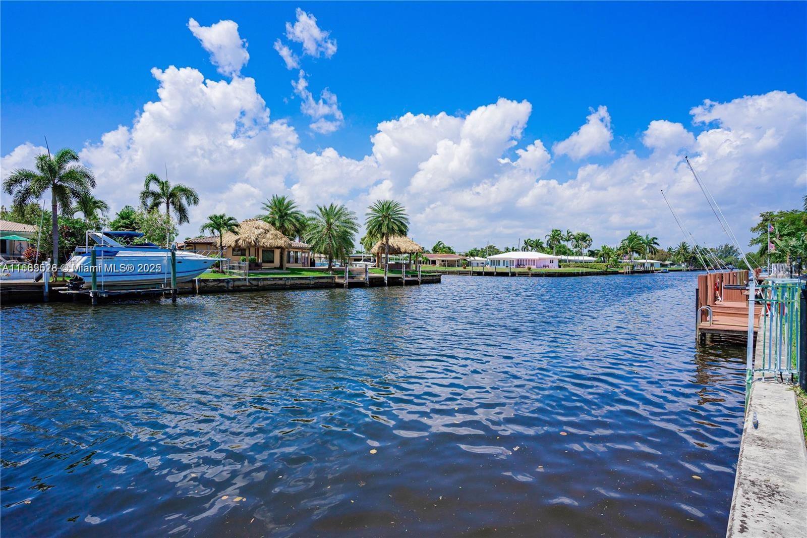 A canal view features a docked boat, palm trees, and waterfront homes under a blue sky — 840 Pine Dr # 103, Pompano Beach FL 33060, POMPANO BEACH, FL