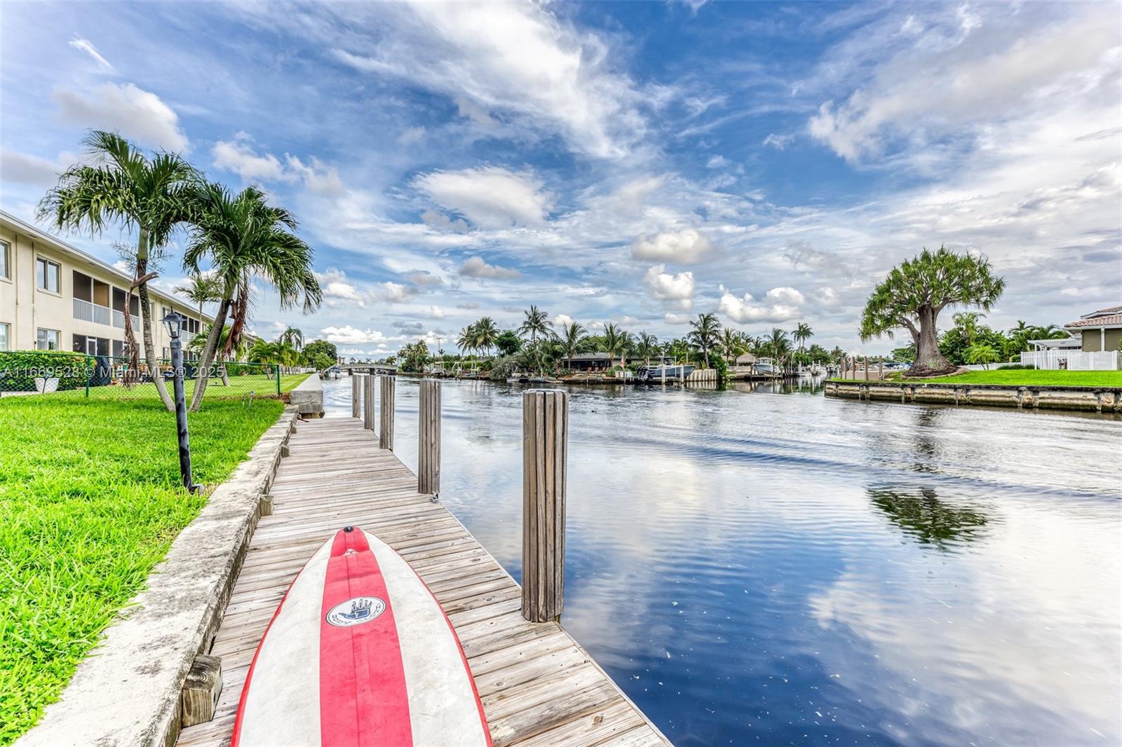 A wooden dock extends into a canal with a paddleboard in the foreground — 840 Pine Dr # 103, Pompano Beach FL 33060, POMPANO BEACH, FL