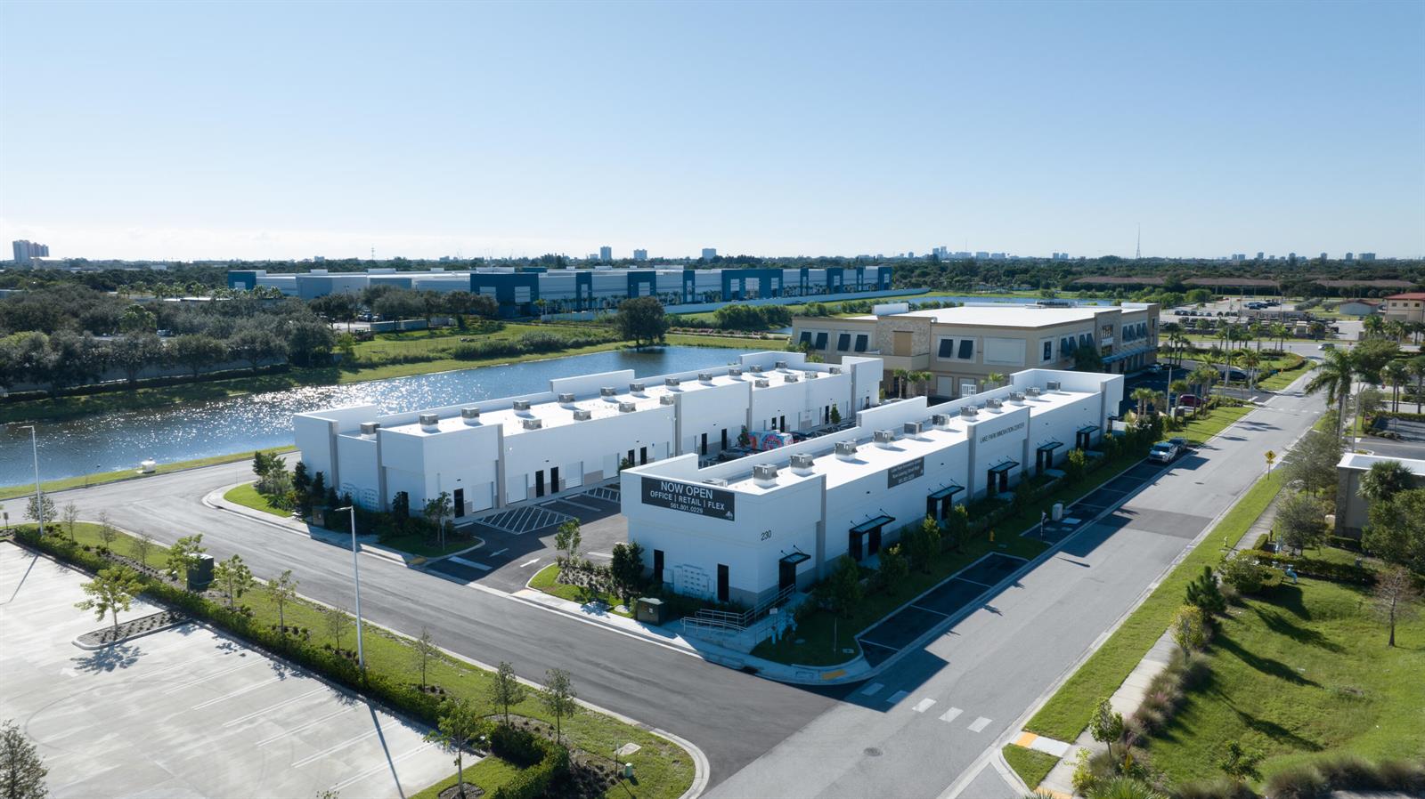 An aerial view shows a modern white commercial building complex with a nearby pond — 230 N Congress Avenue, Lake Park FL 33403, LAKE PARK, FL
