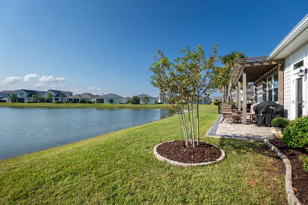 A patio with a pergola overlooks a pond behind a house with a small tree — 9 LOS LAGOS BOULEVARD, PALM COAST, FL