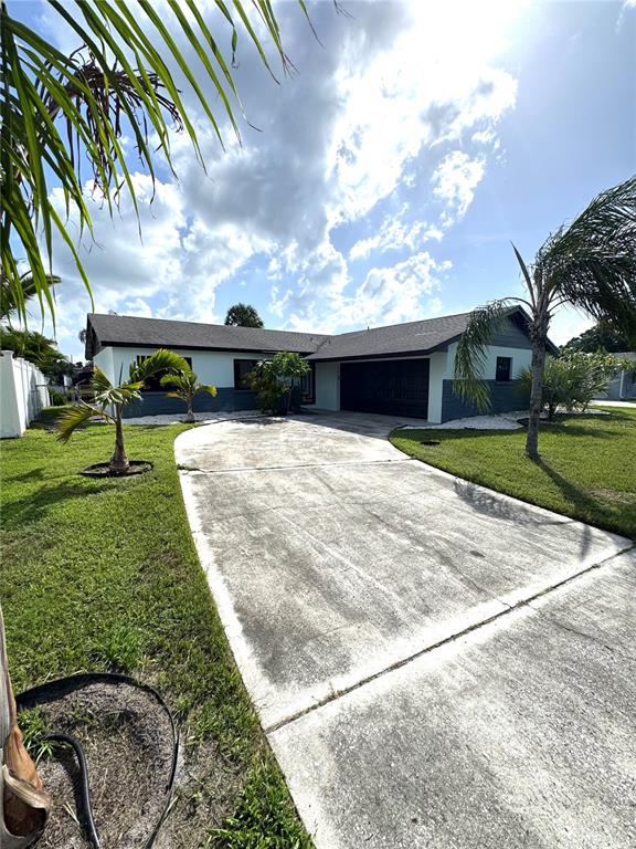 A single-story house with a concrete driveway, a dark roof, and palm trees in the yard — 10708 DONBRESE AVENUE, TAMPA, FL