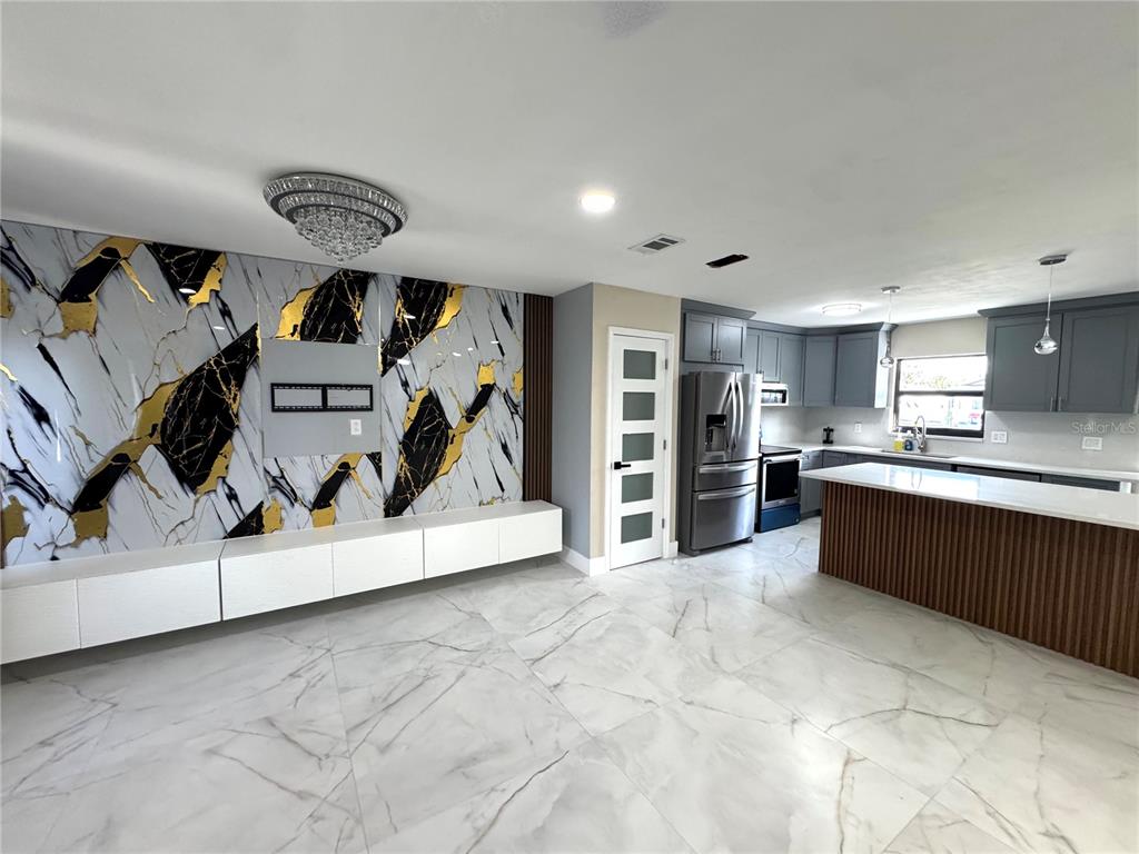 A modern open-concept kitchen and living area features marble-patterned flooring and a bold accent wall — 10708 DONBRESE AVENUE, TAMPA, FL