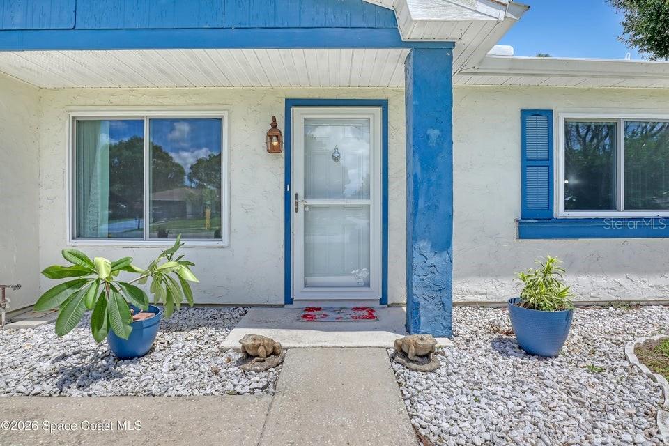 The exterior of a house features a white stucco facade, blue trim, and a front door — 1671 CHARLES BOULEVARD NE, PALM BAY, FL