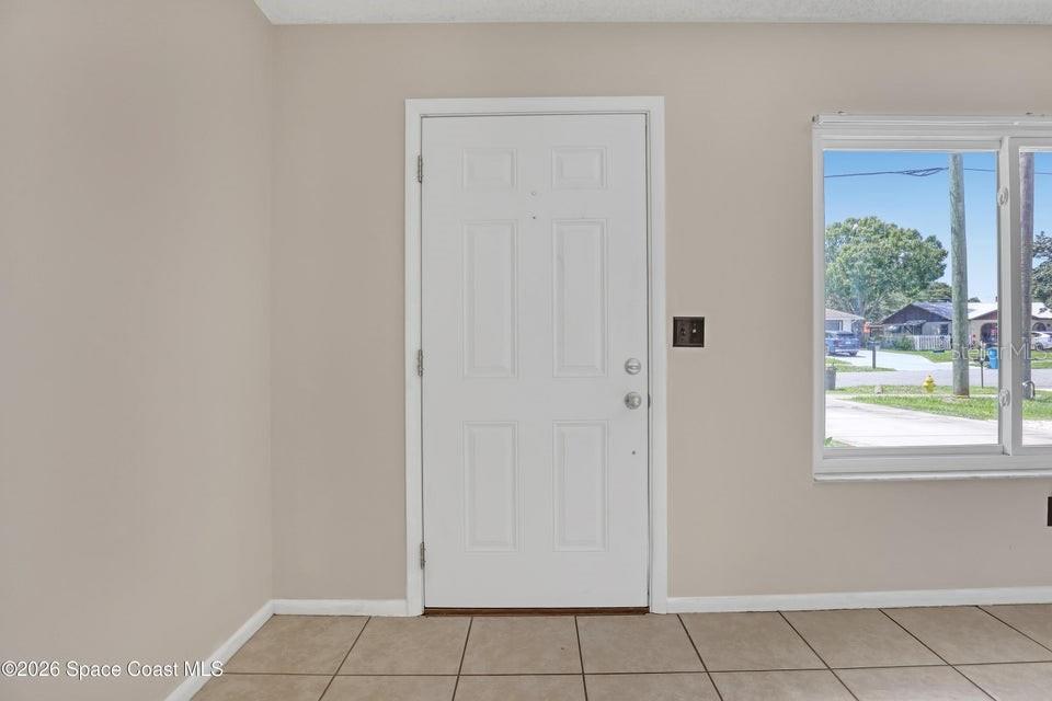 A white front door is centered on a beige wall with tiled flooring — 1671 CHARLES BOULEVARD NE, PALM BAY, FL