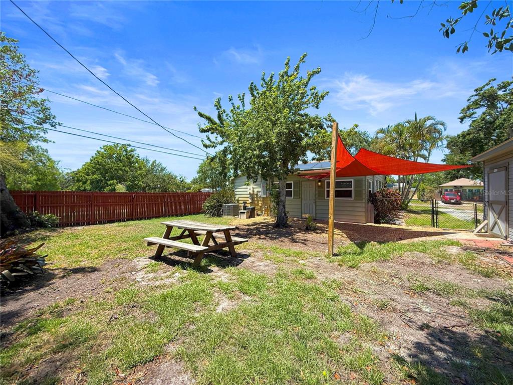 A backyard features a wooden picnic table, a red shade sail, and a wooden fence — 5326 18TH AVENUE S, GULFPORT, FL