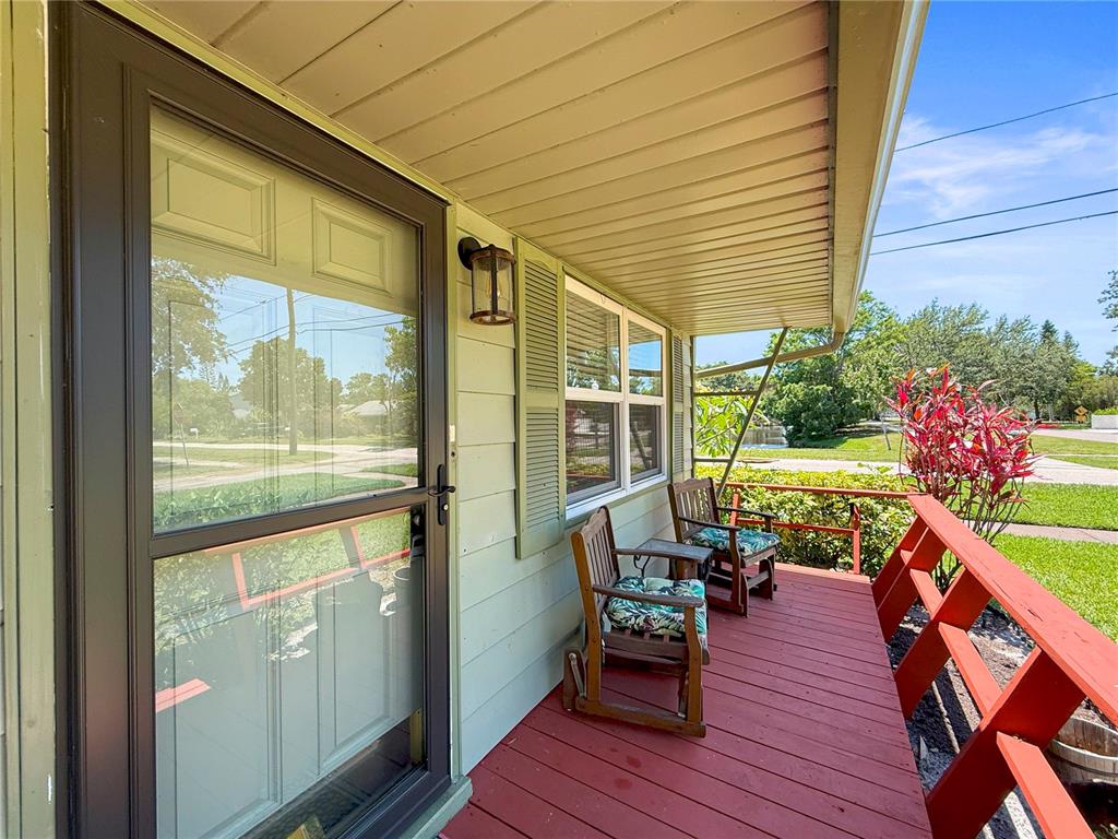A covered front porch features a red wooden deck, two chairs, and light green siding — 5326 18TH AVENUE S, GULFPORT, FL