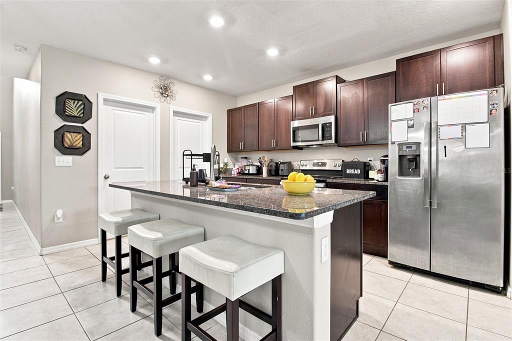 A kitchen with dark wood cabinets, granite countertops, a center island, and stainless steel appliances — 31746 BARREL WAVE WAY, WESLEY CHAPEL, FL
