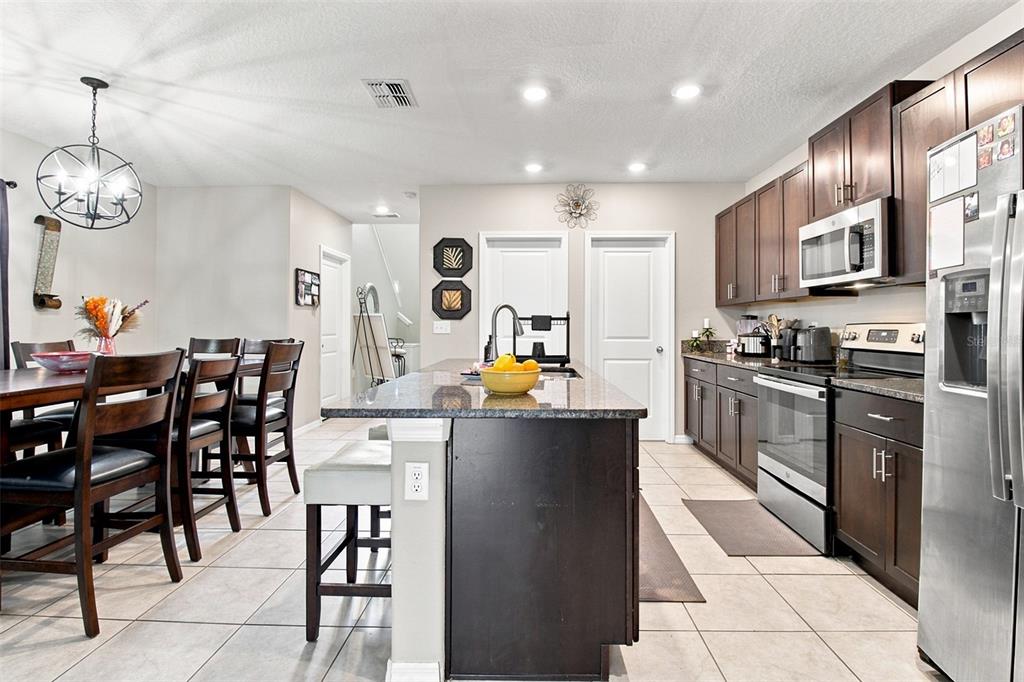 A kitchen with dark wood cabinets, granite countertops, a center island, and an adjacent dining area — 31746 BARREL WAVE WAY, WESLEY CHAPEL, FL