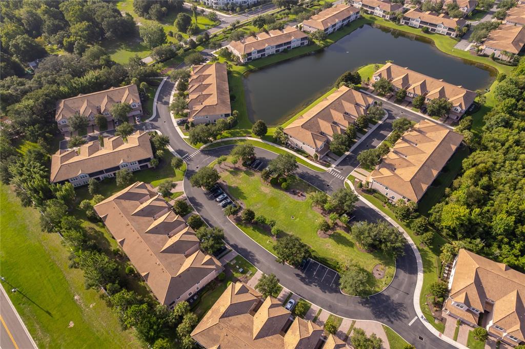 An aerial view shows multiple multi-story apartment buildings with brown roofs surrounding a central pond — 8301 BELLA VIDA CIRCLE UNIT 8301, DAVENPORT, FL