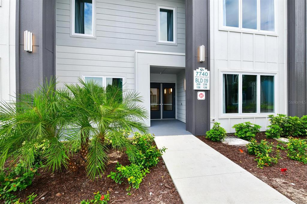 The exterior of a modern multi-story apartment building features a concrete walkway and landscaping — 7740 SANDY RIDGE DRIVE UNIT 136, REUNION, FL