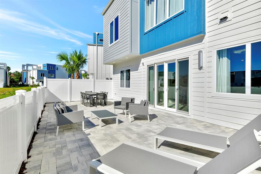 A paved patio with outdoor furniture sits behind a white house with blue accents — 7740 SANDY RIDGE DRIVE UNIT 136, REUNION, FL