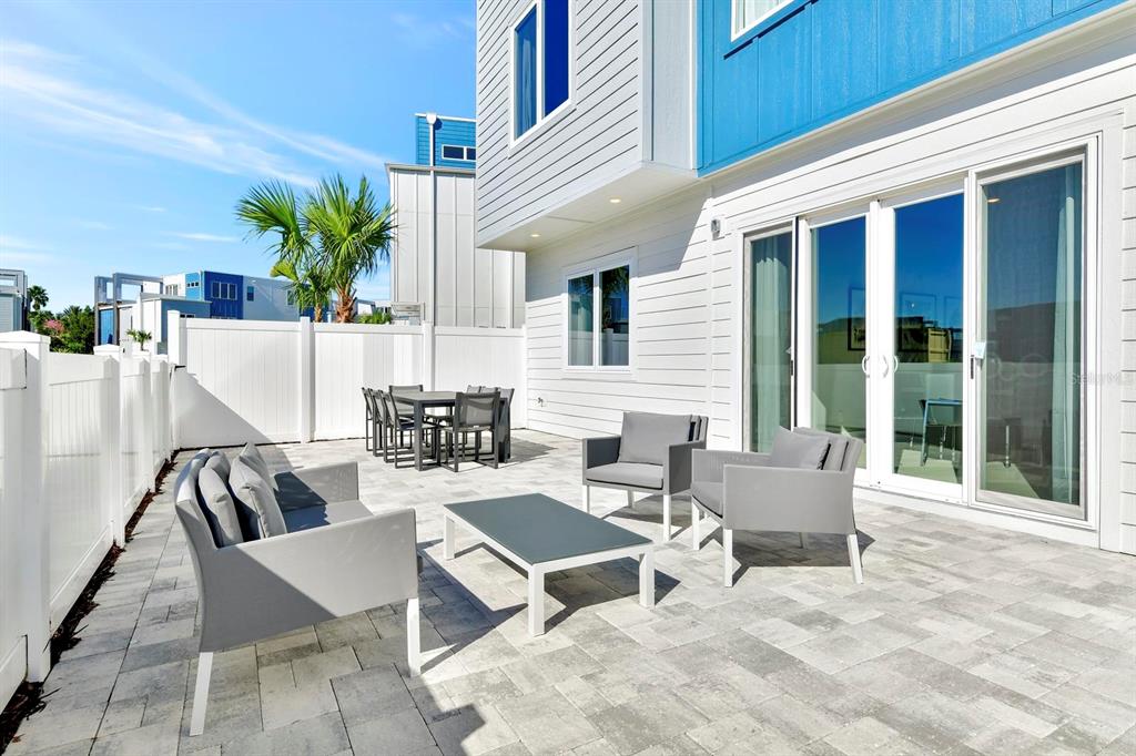 A paved outdoor patio features modern gray furniture, a dining set, and a white fence — 7740 SANDY RIDGE DRIVE UNIT 136, REUNION, FL