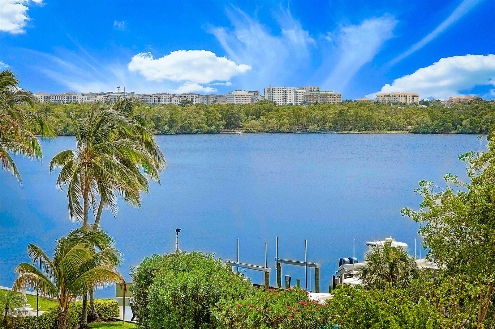A view of a lake with a boat dock, palm trees, and distant buildings — 2121 N Ocean Boulevard # 407w, Boca Raton FL 33431, BOCA RATON, FL