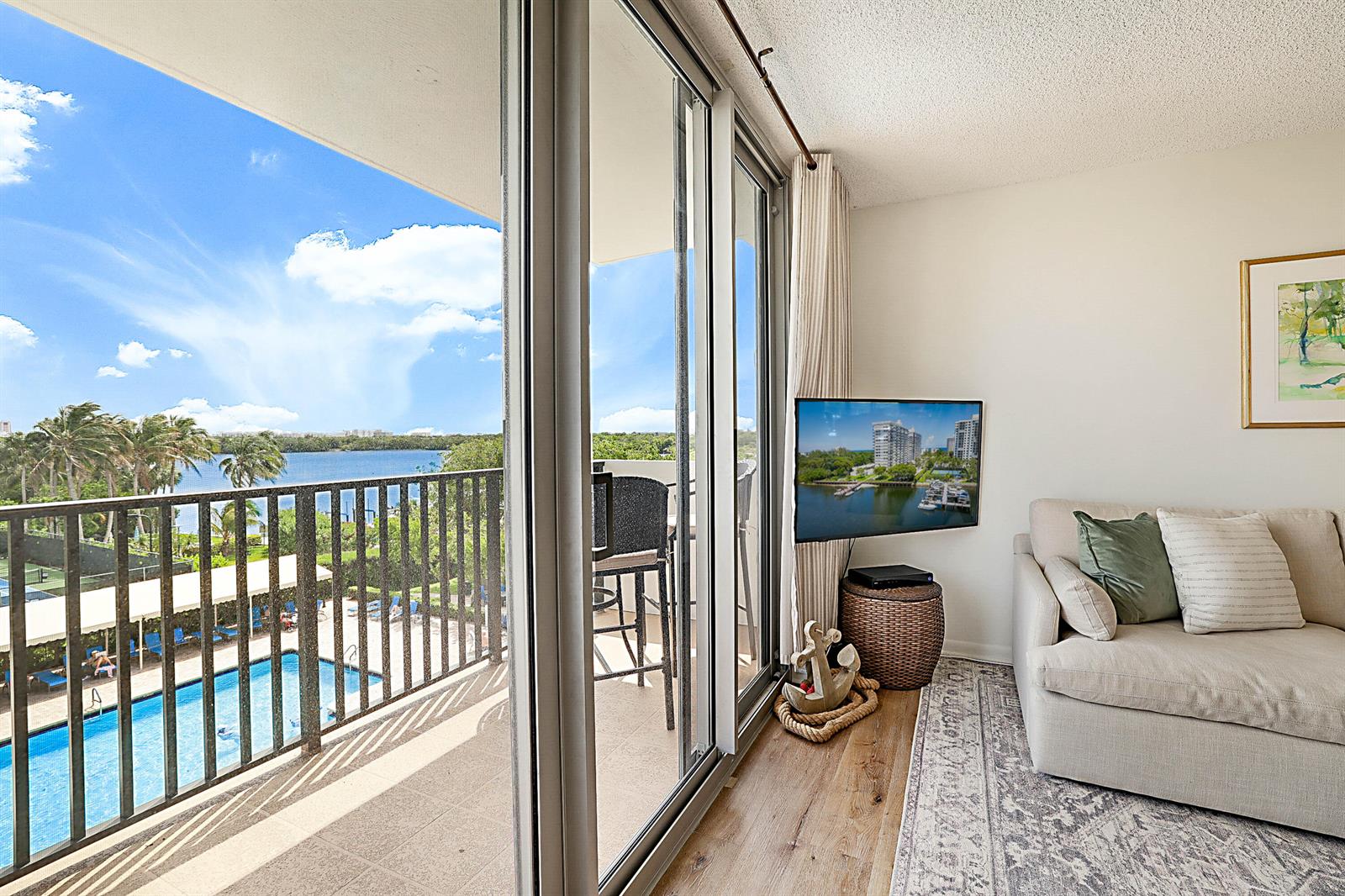 A living room with a beige sofa, wood floors, and a balcony overlooking a pool — 2121 N Ocean Boulevard # 407w, Boca Raton FL 33431, BOCA RATON, FL