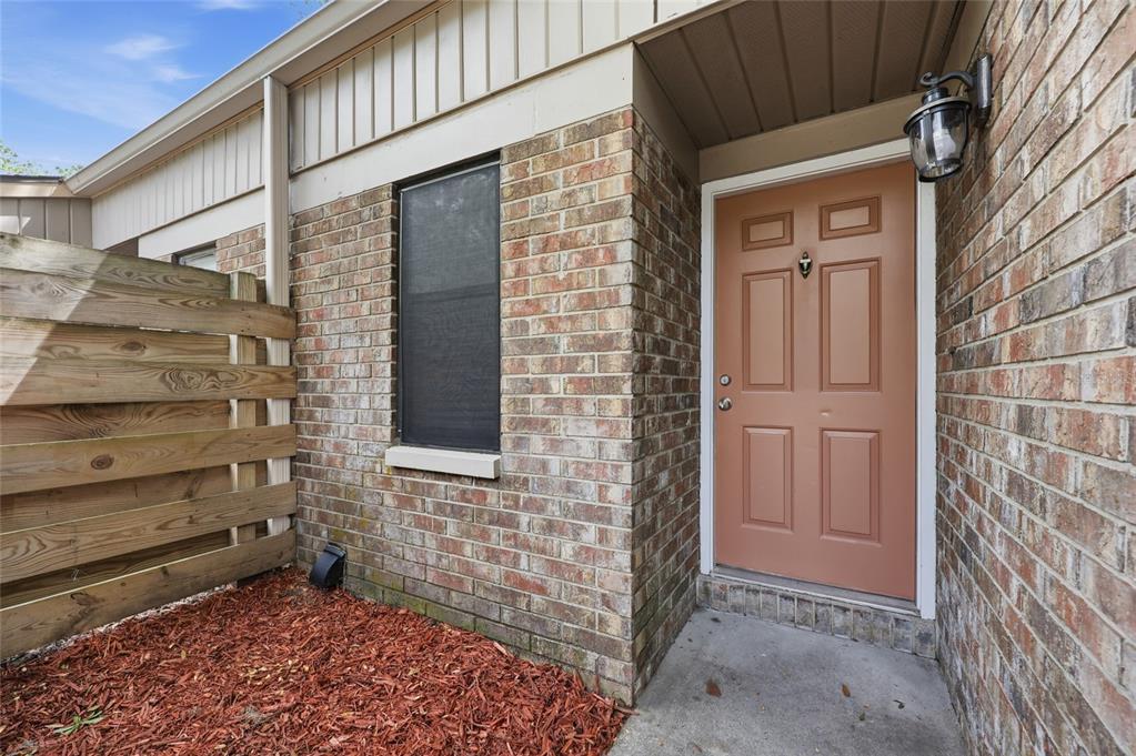 A brick exterior wall features a tan front door, a window, and a wooden privacy fence — 3405 NW 52ND TERRACE, GAINESVILLE, FL