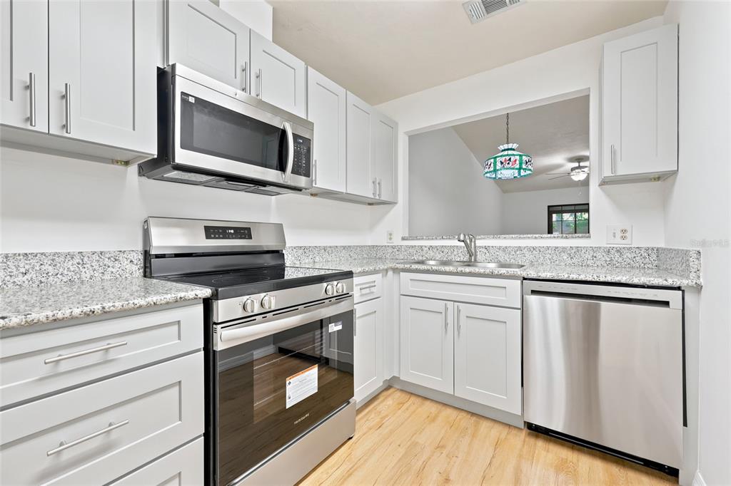 A kitchen with white cabinets, stainless steel appliances, granite countertops, and light wood flooring — 3405 NW 52ND TERRACE, GAINESVILLE, FL