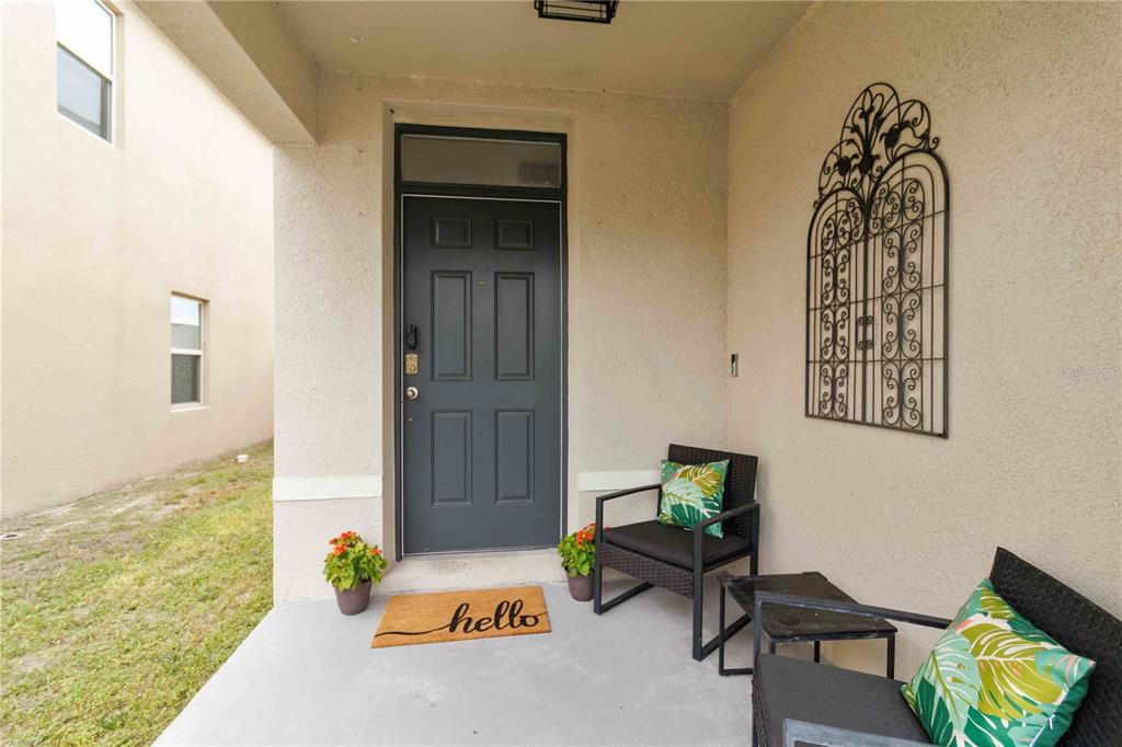 A covered front porch features a dark gray door, two chairs, and a decorative wall hanging — 10230 GEESE TRAIL CIRCLE, SUN CITY CENTER, FL