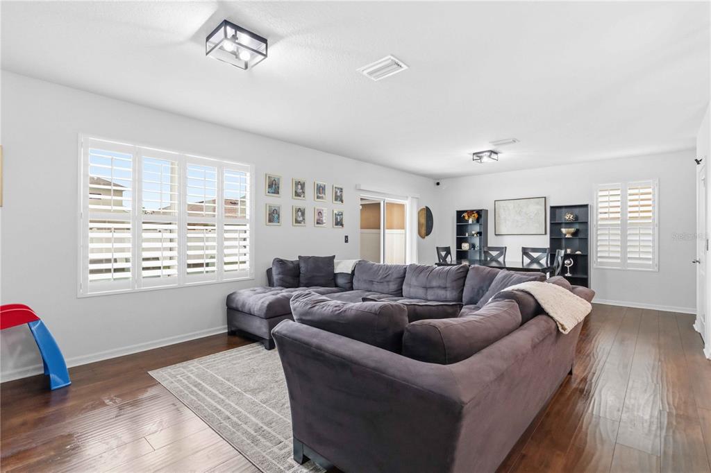 A living room features a large gray sectional sofa, hardwood floors, and plantation shutters — 10230 GEESE TRAIL CIRCLE, SUN CITY CENTER, FL
