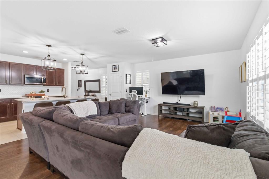A living room with a large sectional sofa faces a wall-mounted television and kitchen — 10230 GEESE TRAIL CIRCLE, SUN CITY CENTER, FL