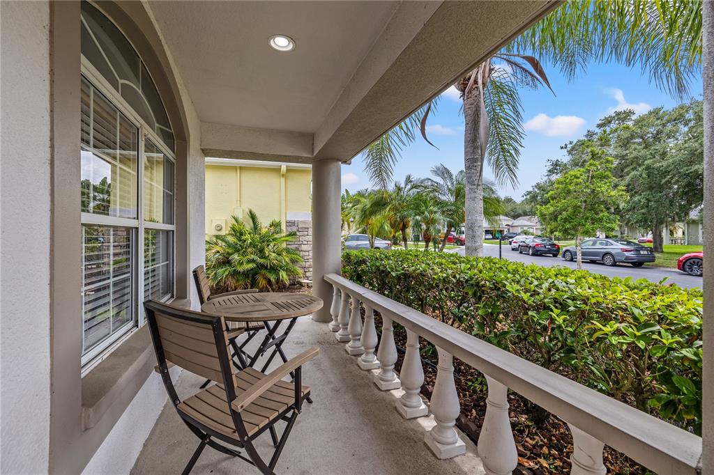 A covered porch features a small table with two chairs, a balustrade railing, and landscaping — 3056 SUNWATCH DRIVE, WESLEY CHAPEL, FL