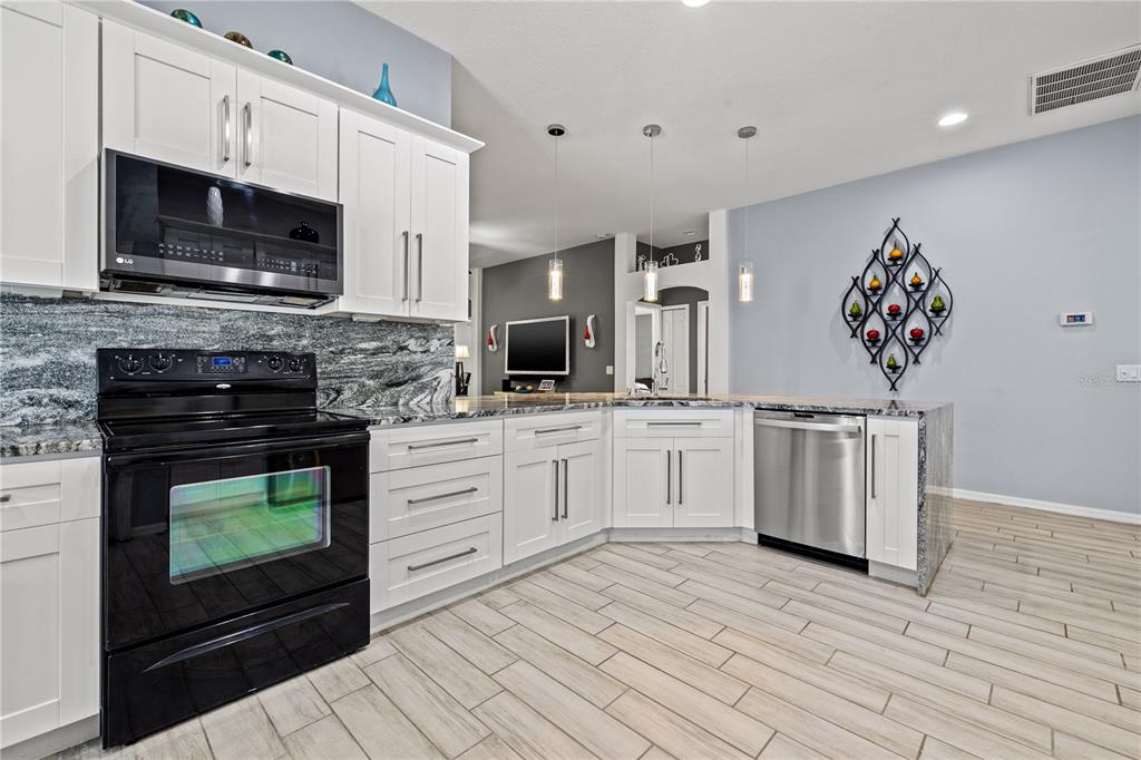 A kitchen features white cabinets, black appliances, granite countertops, and light-colored wood-look tile flooring — 3056 SUNWATCH DRIVE, WESLEY CHAPEL, FL