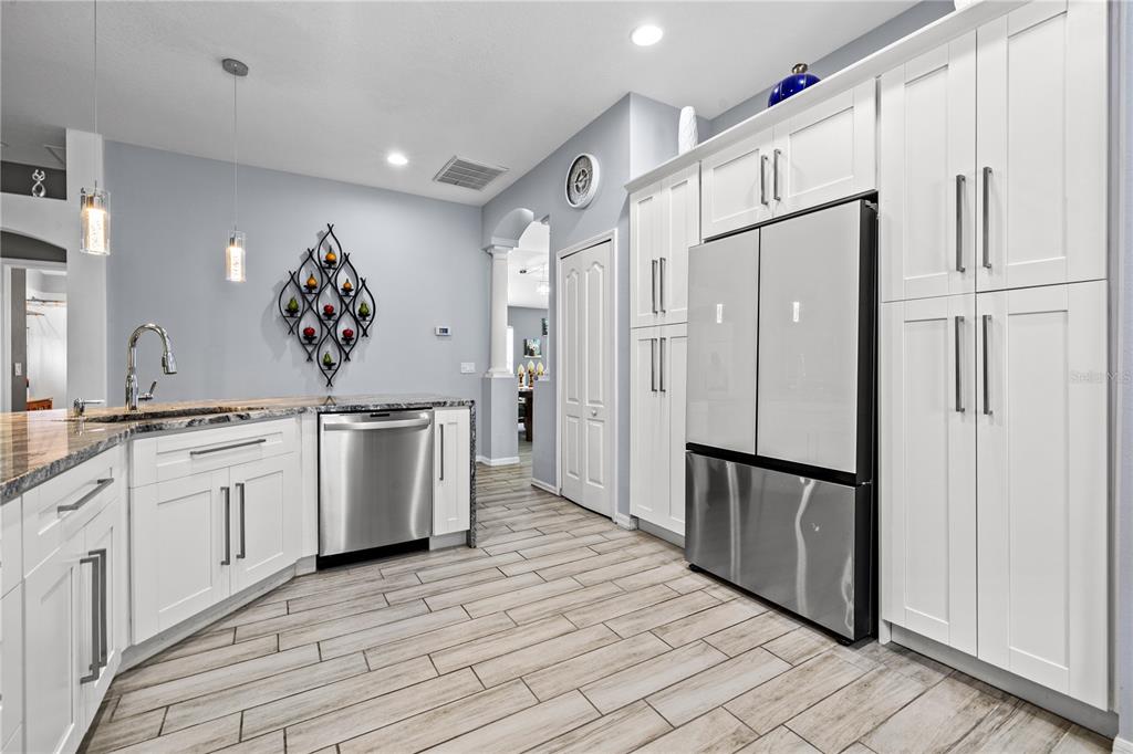A kitchen features white cabinetry, stainless steel appliances, granite countertops, and light wood-look tile flooring — 3056 SUNWATCH DRIVE, WESLEY CHAPEL, FL