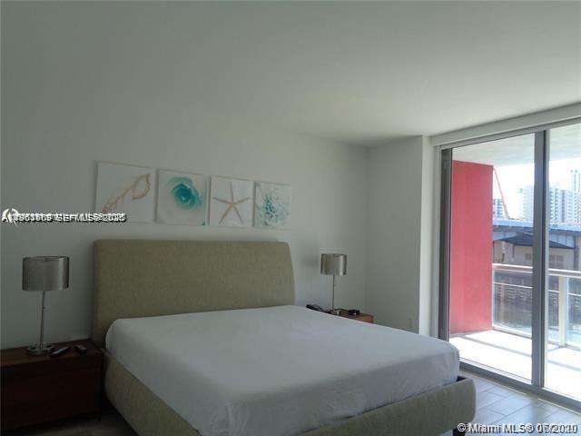 A bedroom features a bed with a light-colored headboard, two lamps, and a balcony view — 2600 E Hallandale Beach Blvd # T301, Hallandale Beach FL 33009, HALLANDALE BEACH, FL